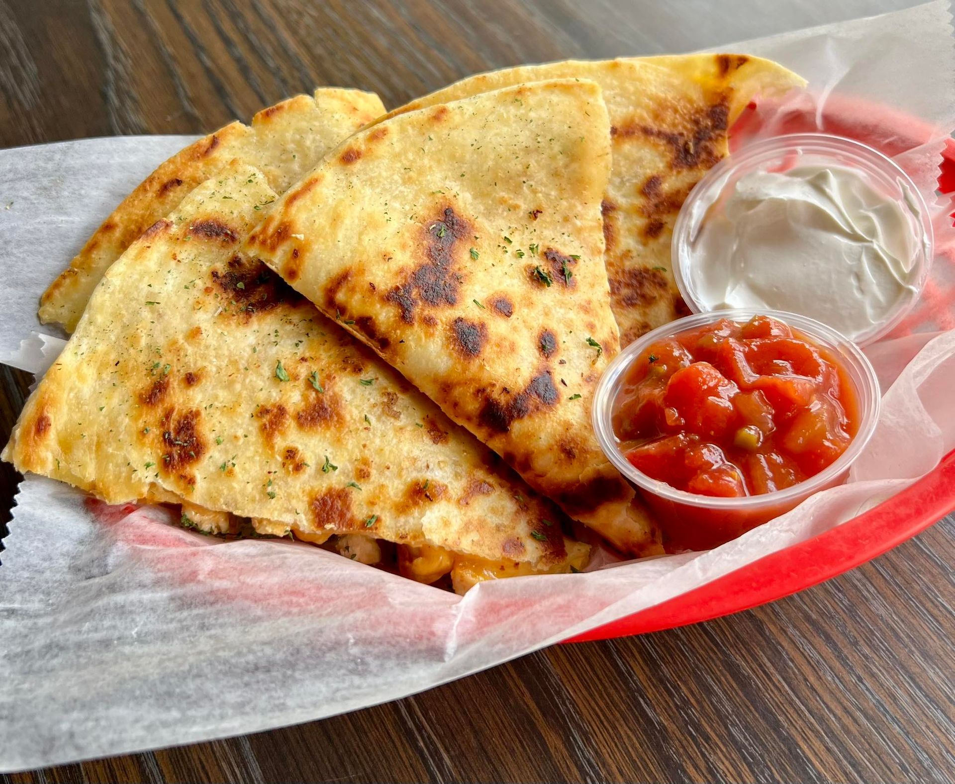 Quesadillas with salsa and sour cream in a red basket on a table.