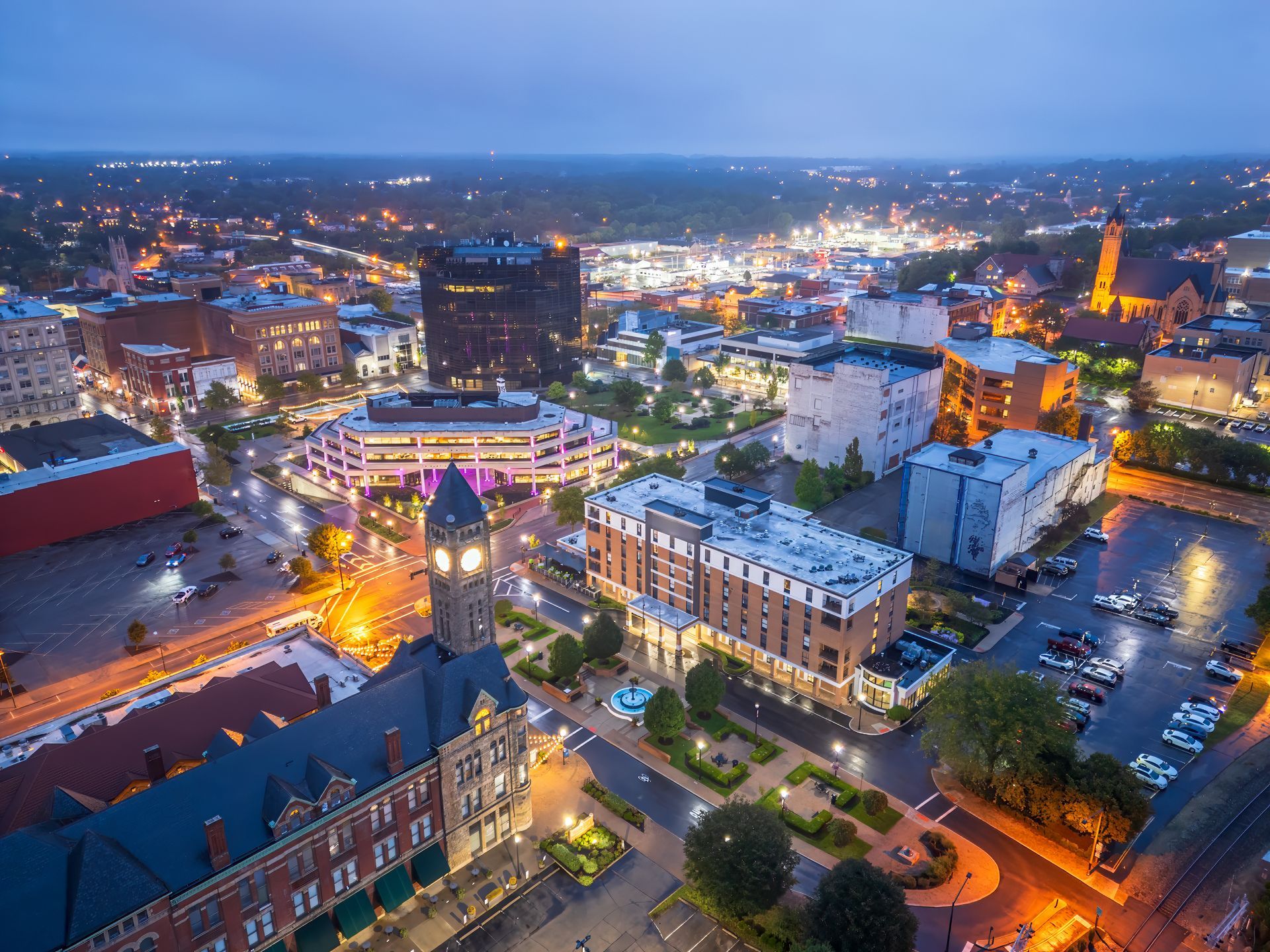 Aerial cityscape at dusk with glowing streetlights, buildings, and a busy downtown grid.
