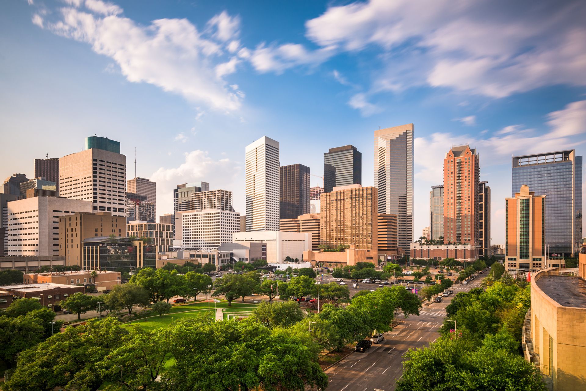 Houston city skyline with skyscrapers and green trees under a blue sky.