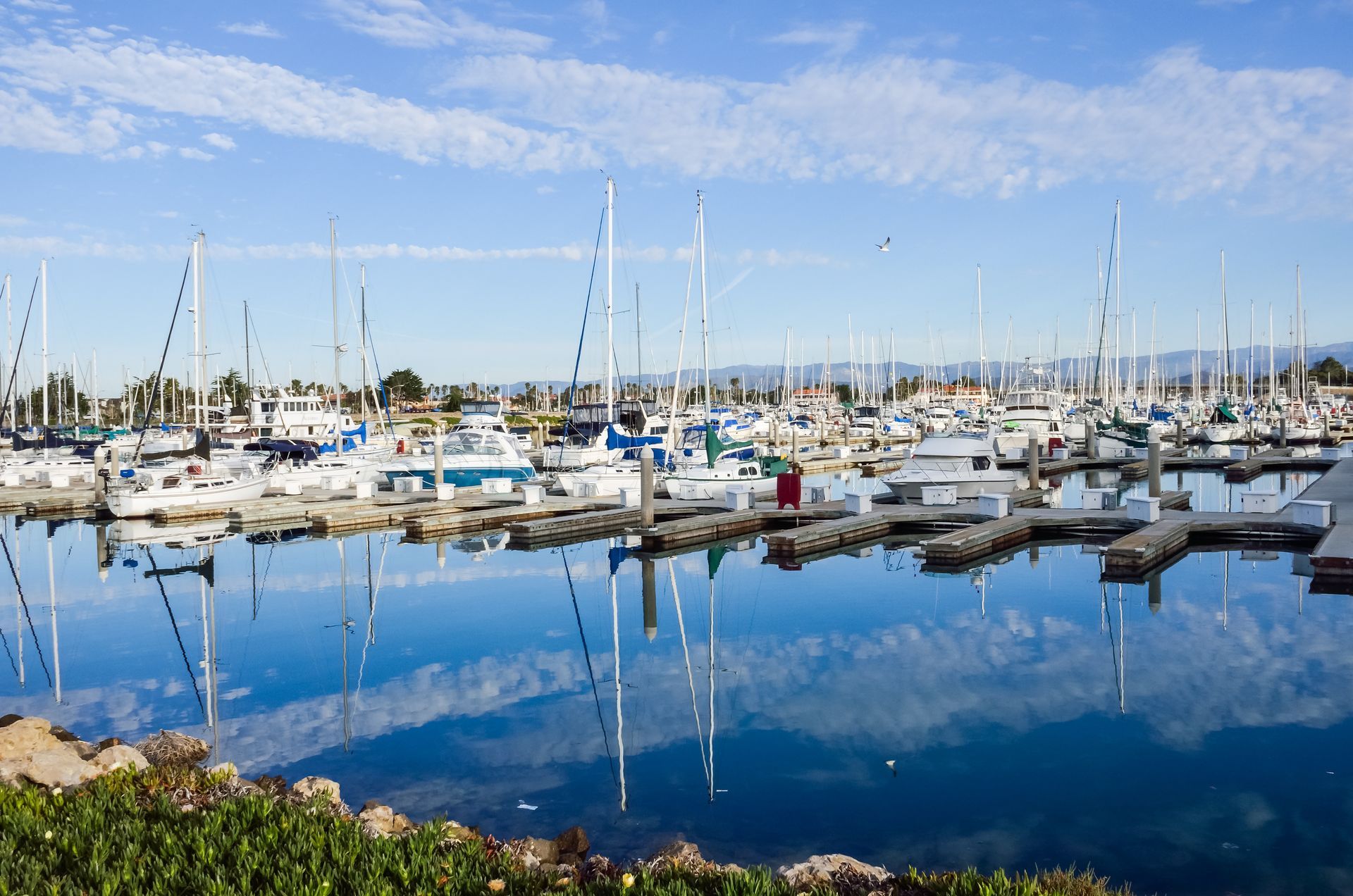 Marina with sailboats and yachts reflected in calm blue water under a clear sky