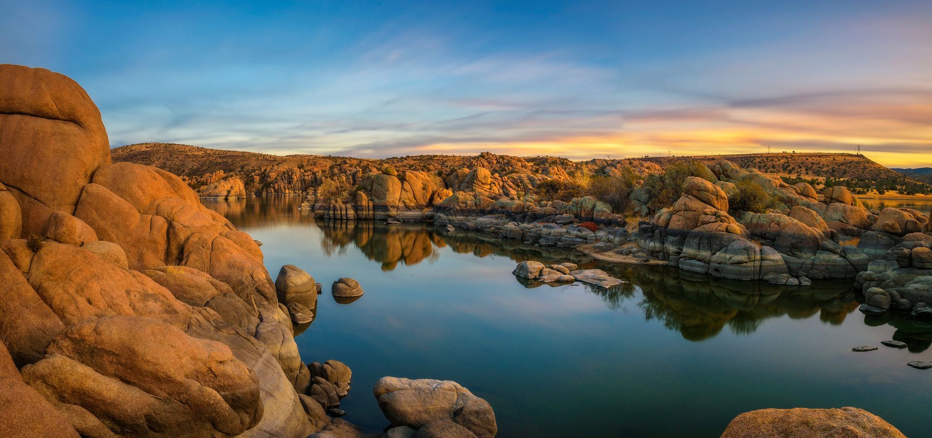 Sunlit rocky canyon with calm water reflecting orange cliffs at sunset