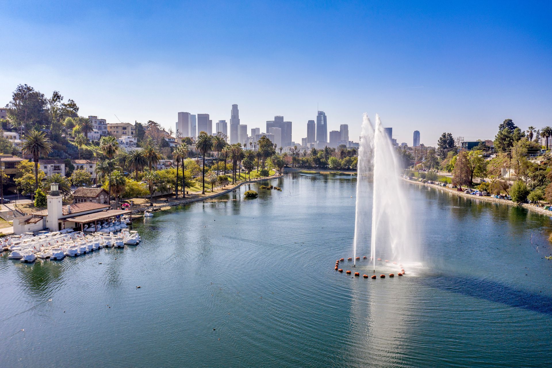 City park lake with a large fountain and downtown skyline in the distance under a clear blue sky