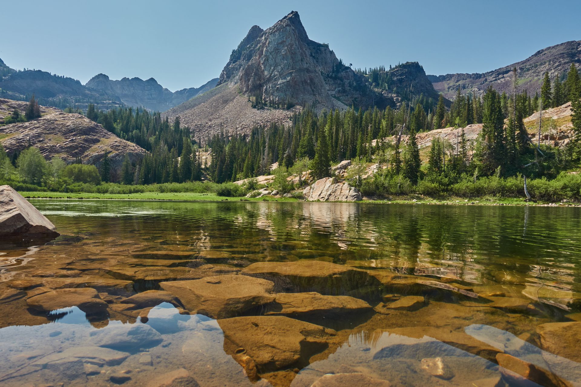 Mountain lake scene with jagged peak, clear water, and trees reflecting in the water.