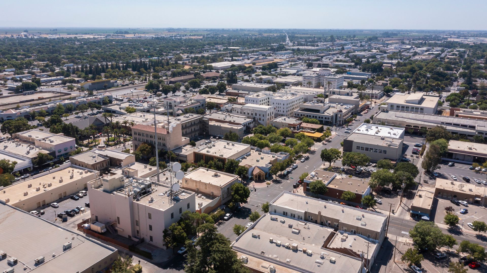 Aerial view of a sprawling town with low-rise buildings, street grids, and scattered trees under a clear blue sky.