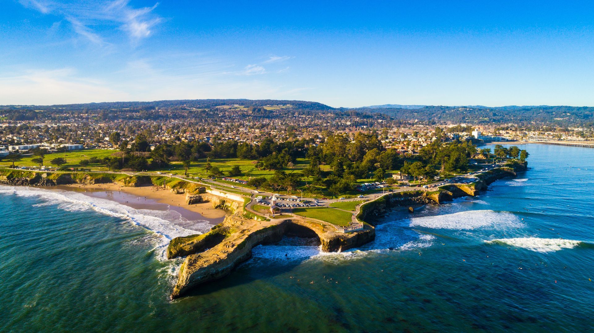 Aerial view of a coastal cliff and beach with turquoise ocean and a city in the distance