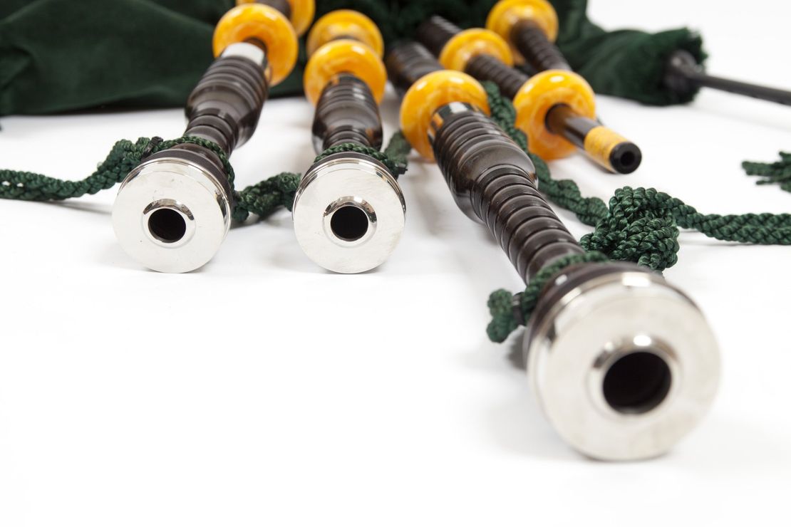 A close up of a pair of bagpipe pipes with silver mounts on a white surface.