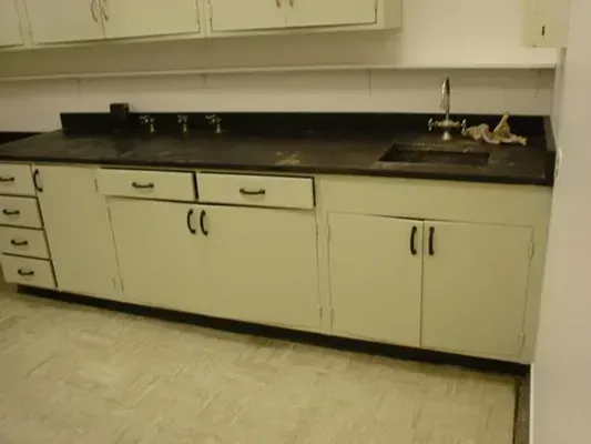A laboratory with white cabinets, black countertop, and a sink.