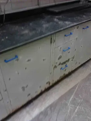 Laboratory cabinet with damaged metal exterior, blue handles, and a dark countertop.