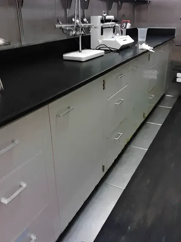 Laboratory counter with drawers, equipment on a black surface, and a dark floor.