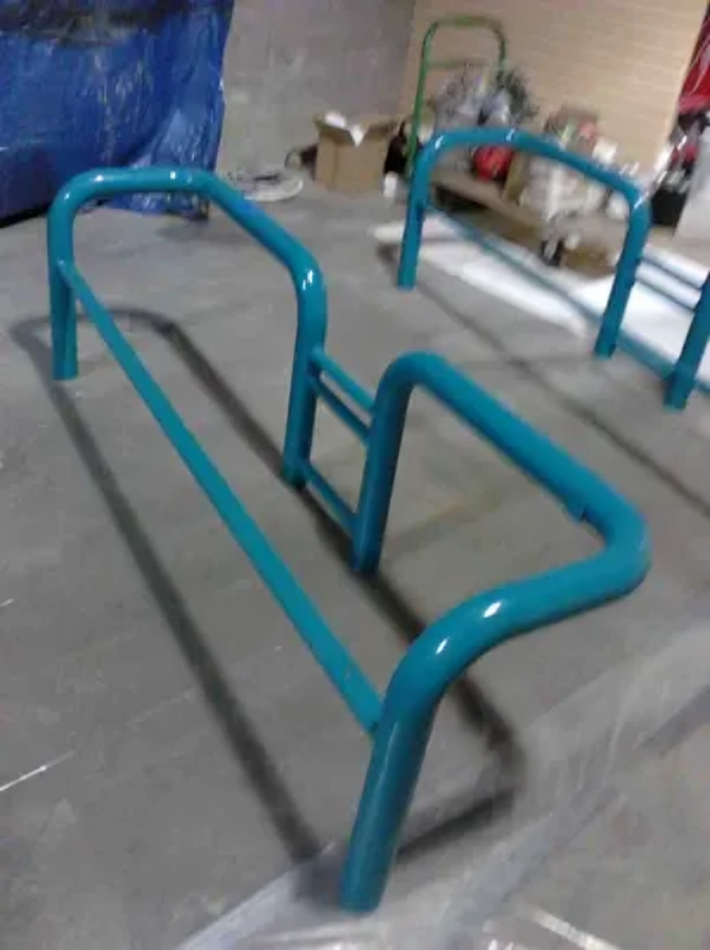 Turquoise metal handrail frame on a gray surface, likely for an accessible ramp or pathway.