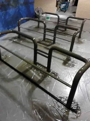 Metal barriers freshly painted black on a plastic sheet, indoors.