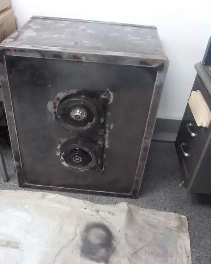 A metal speaker cabinet with two visible speakers, sitting on a surface near a desk.