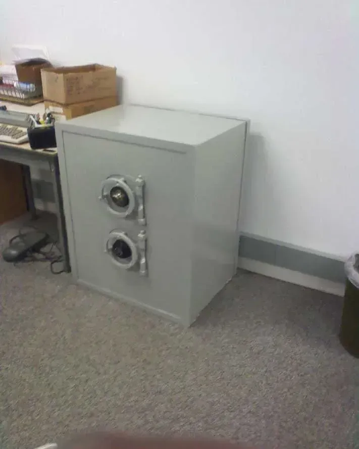 Gray safe in an office setting, with two circular dials on its front.