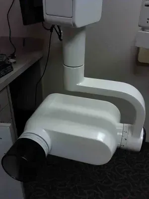 White dental X-ray machine attached to a wall, with a black cone and adjustable arm.