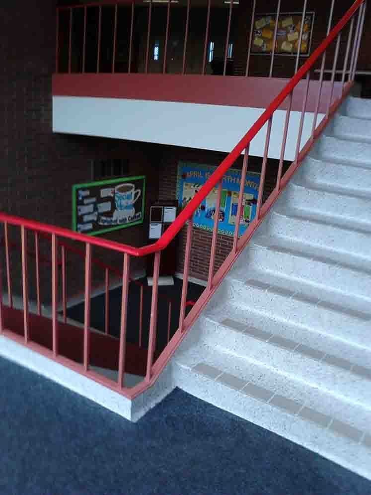 Staircase with red railing, brick wall, and a sign with a cup of coffee in a school.