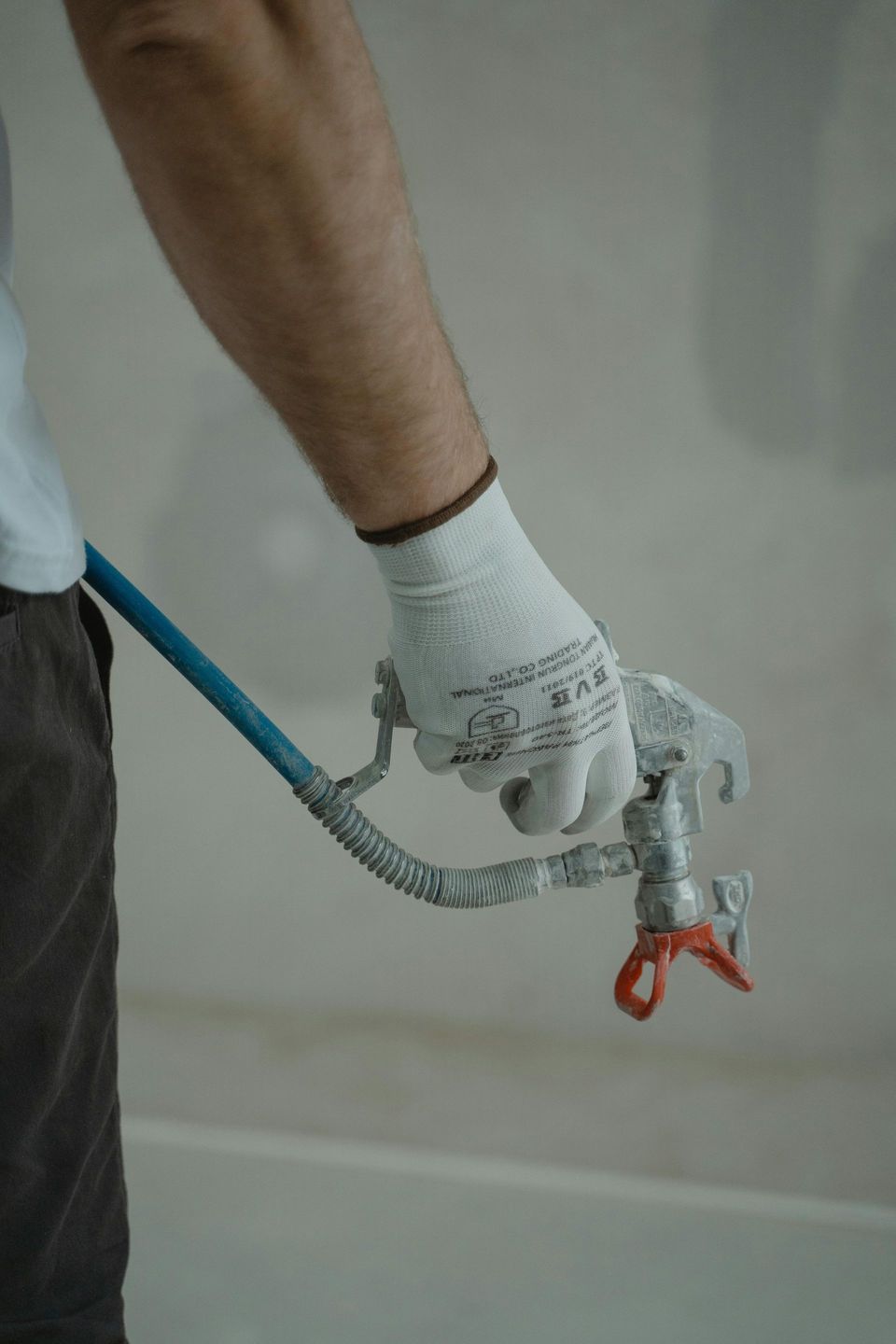 Person wearing work gloves holding a paint sprayer nozzle, indoors.