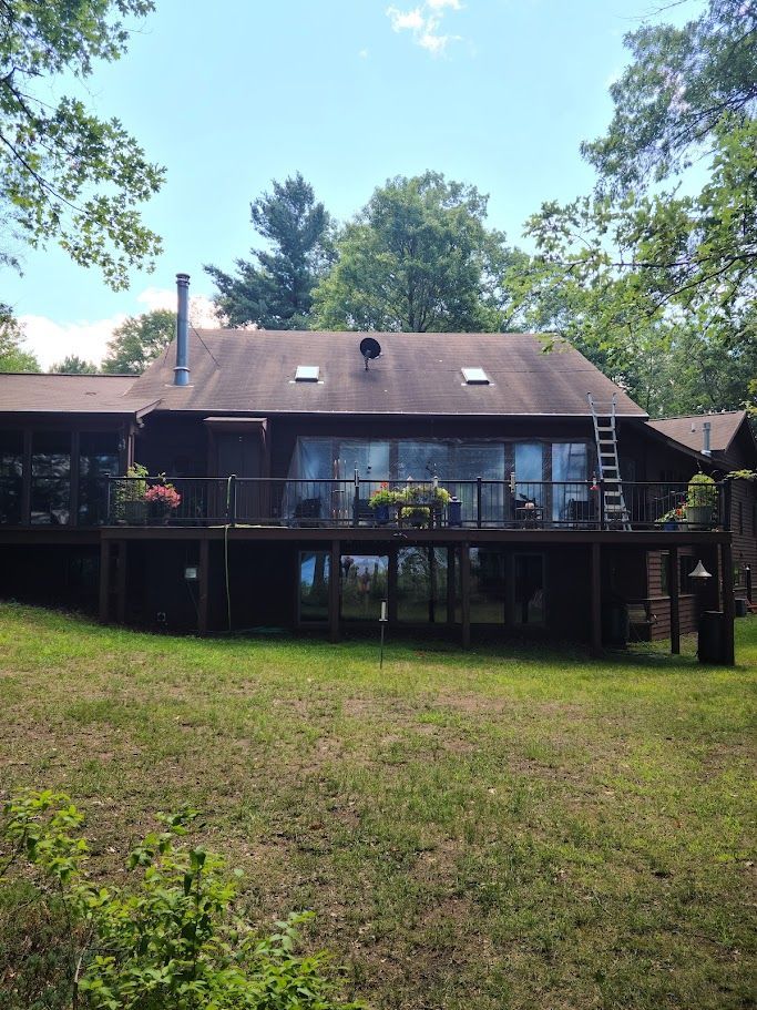 The back of a house with a large deck and a ladder in the grass.
