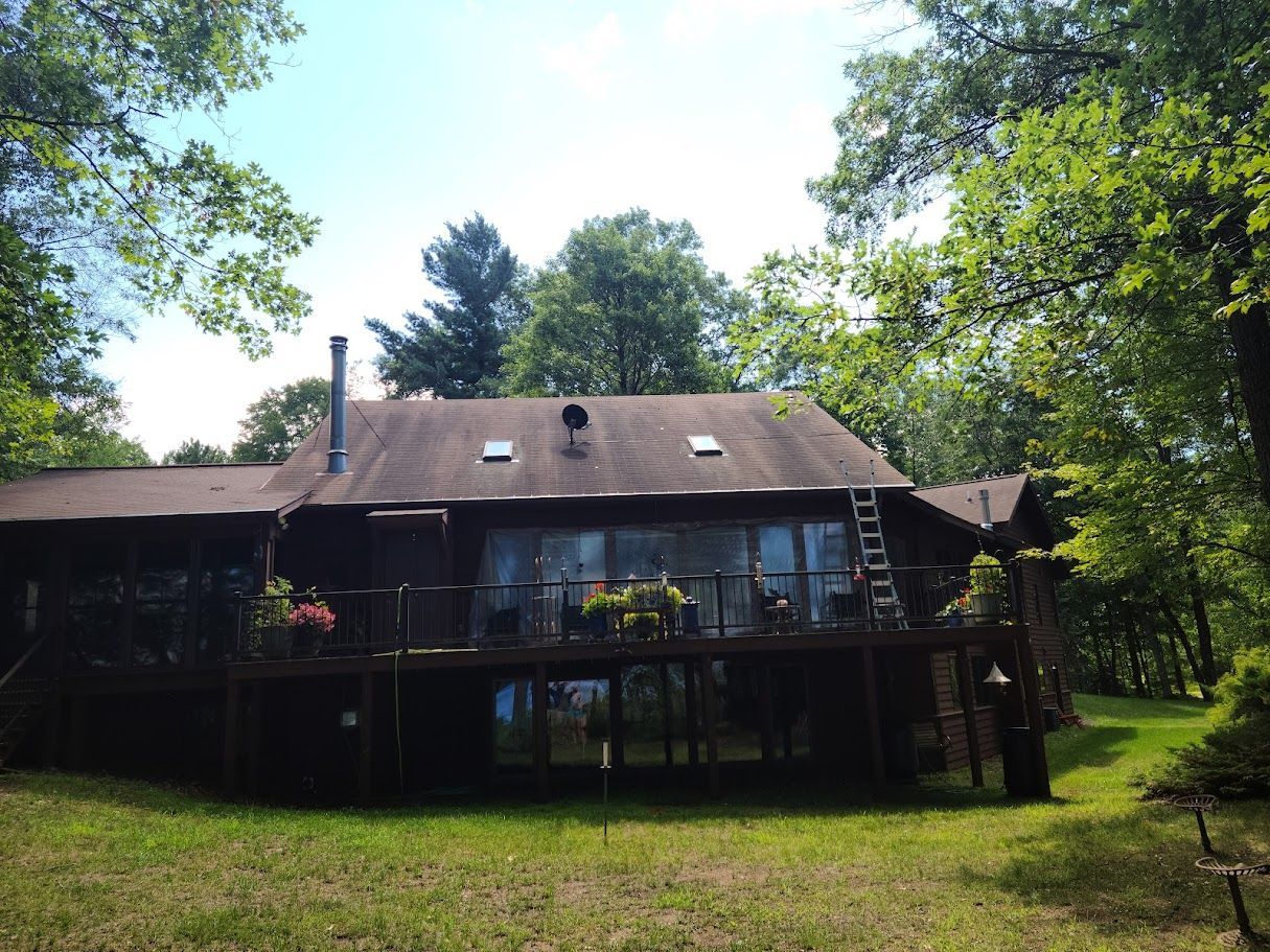 A large house with a large deck is surrounded by trees on a sunny day.