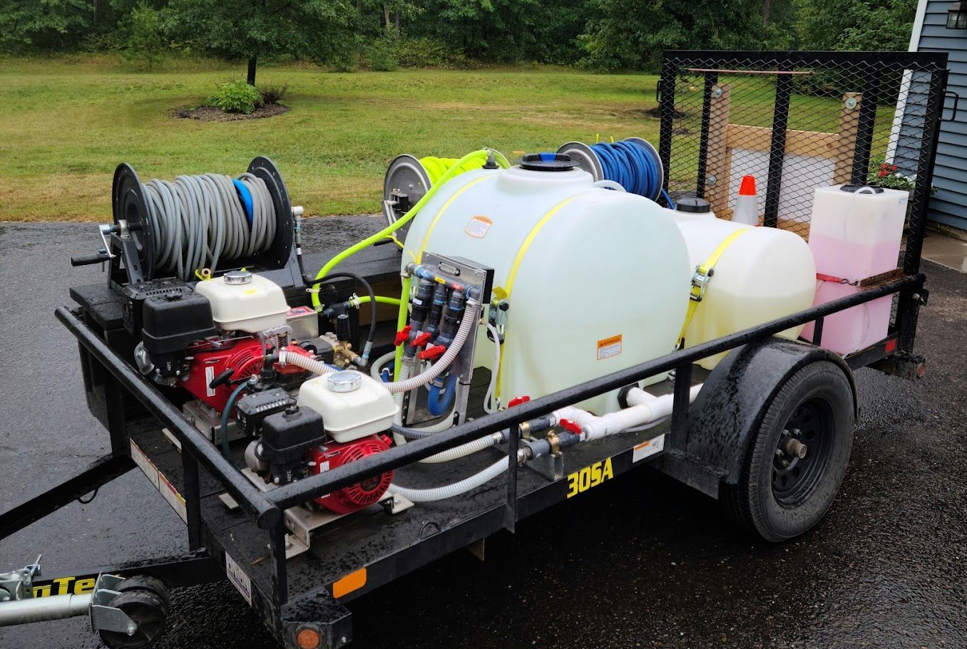 A trailer with a hose and tanks on it is parked in a driveway.