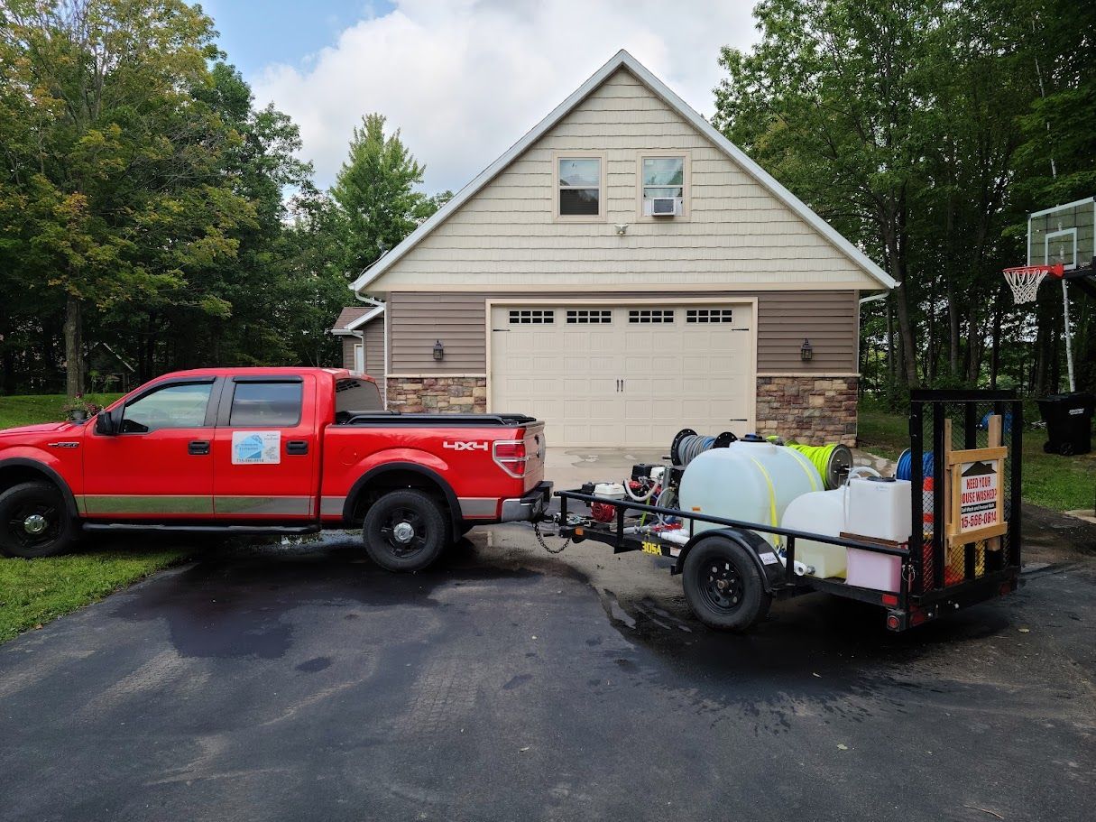 A red truck is parked in front of a house with a trailer attached to it.