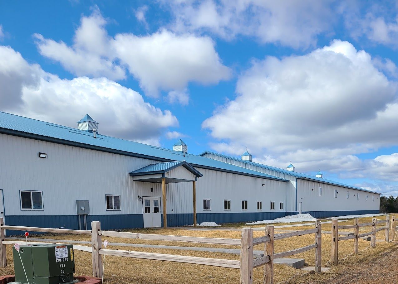 A large white building with a blue roof and a wooden fence in front of it.