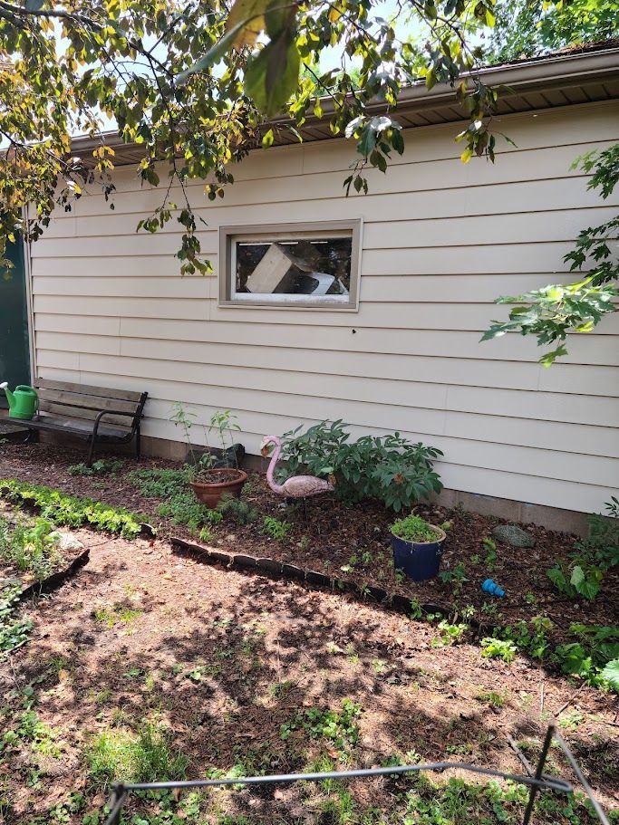 A white house with a window and a garden in front of it.