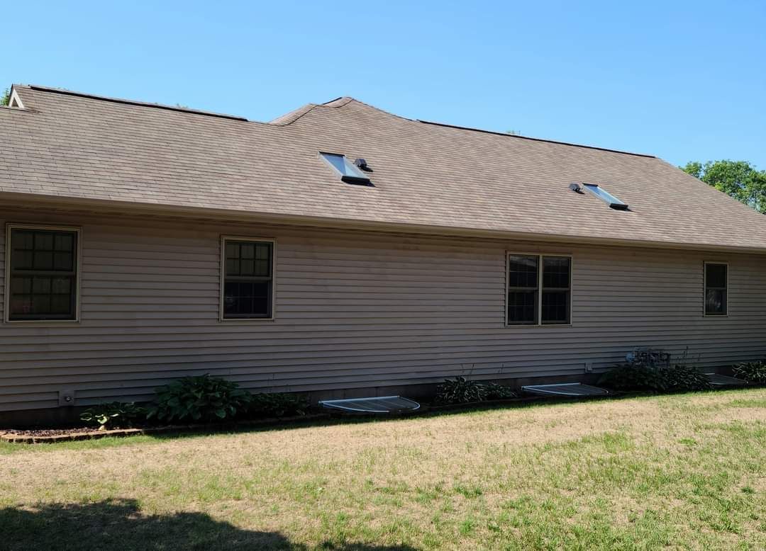 A house with a brown roof and a lot of windows is sitting on top of a lush green field.