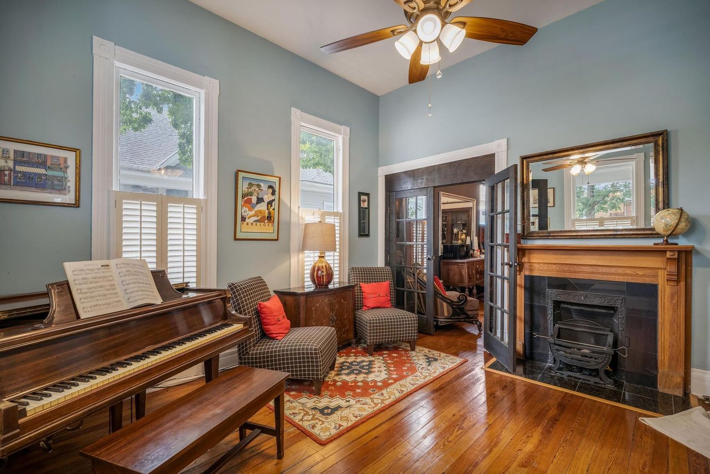 A living room with a piano , chairs , a fireplace and a ceiling fan.