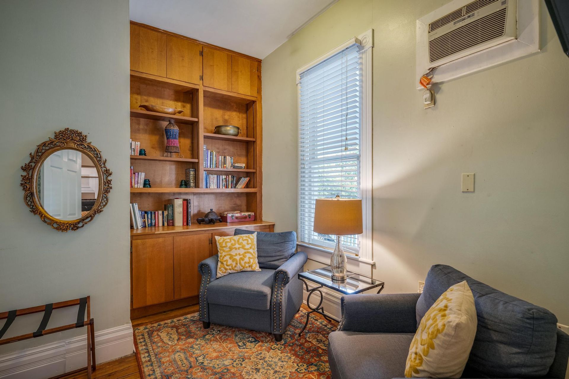 A living room with two chairs , a table , a mirror and a bookshelf.