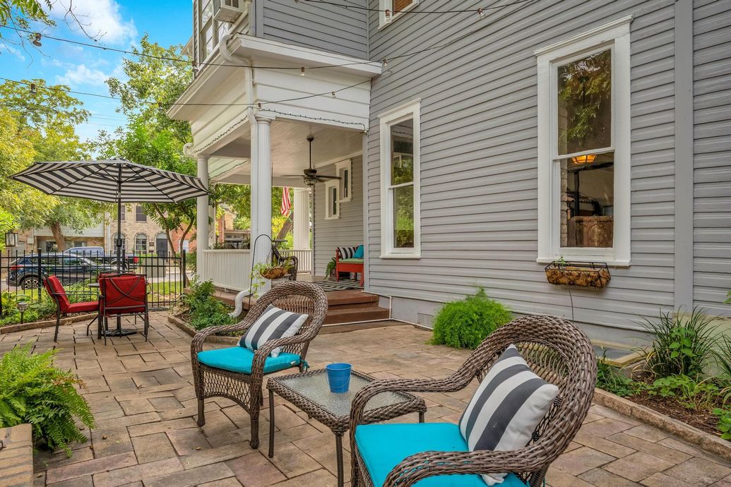 A patio with chairs , a table and an umbrella in front of a house.