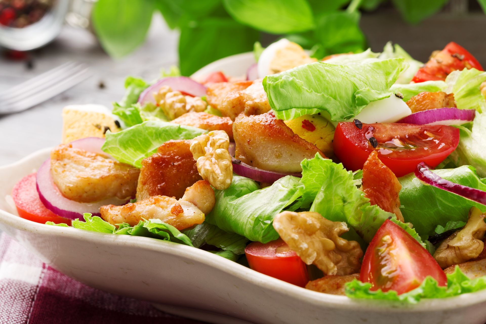 A salad with chicken , lettuce , tomatoes , onions and walnuts on a plate.