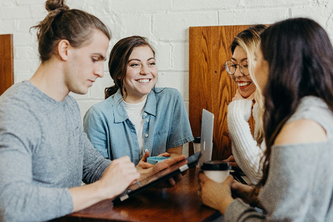 A group of people are sitting around a table looking at a tablet.