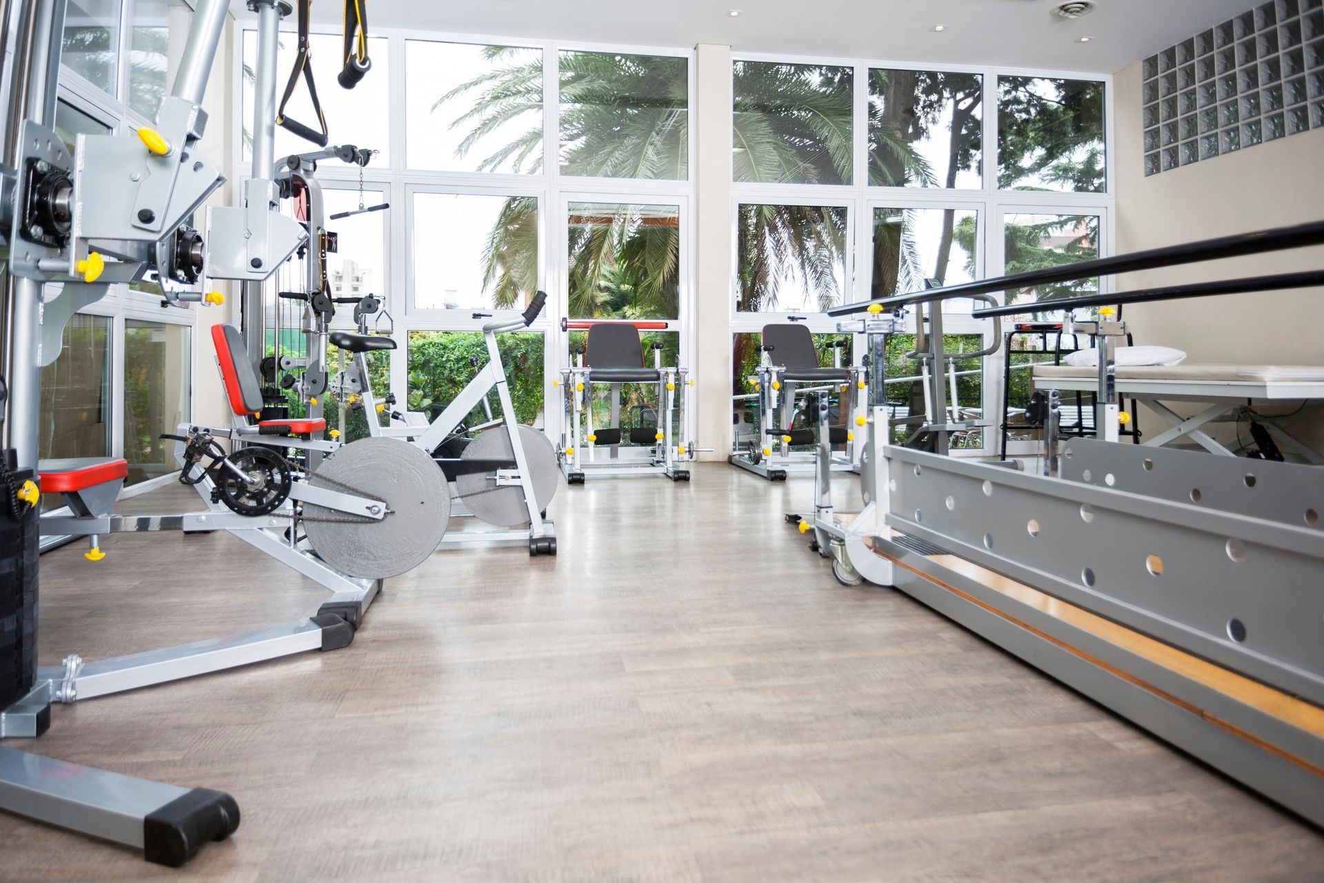 A brightly lit fitness center with exercise machines and parallel bars, viewed from a low angle on a light wood floor. A brightly lit fitness center with exercise machines and parallel bars, viewed from a low angle on a light wood floor.