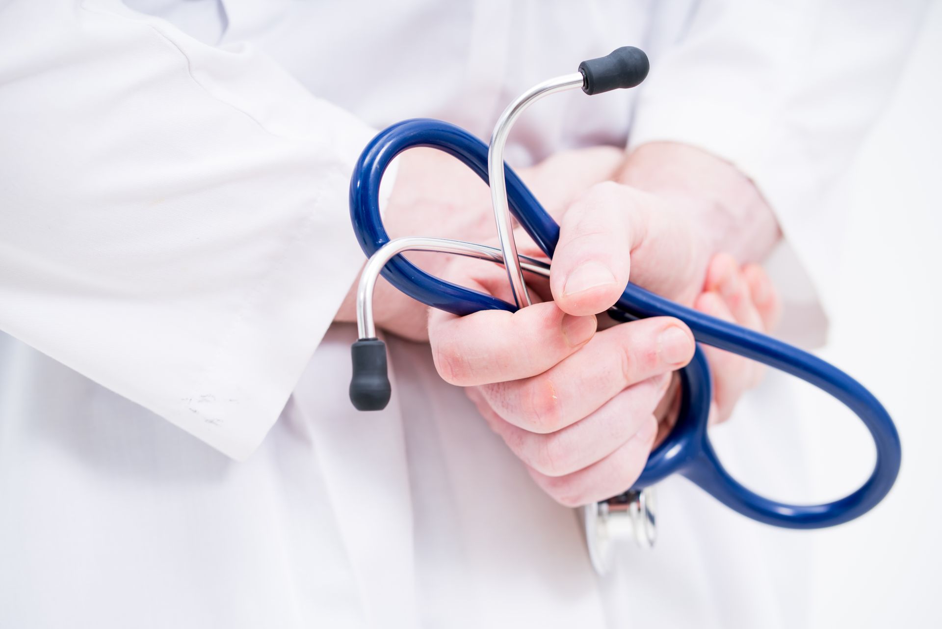 A medical professional in a white coat holds a blue stethoscope in their hands. A medical professional in a white coat holds a blue stethoscope in their hands.