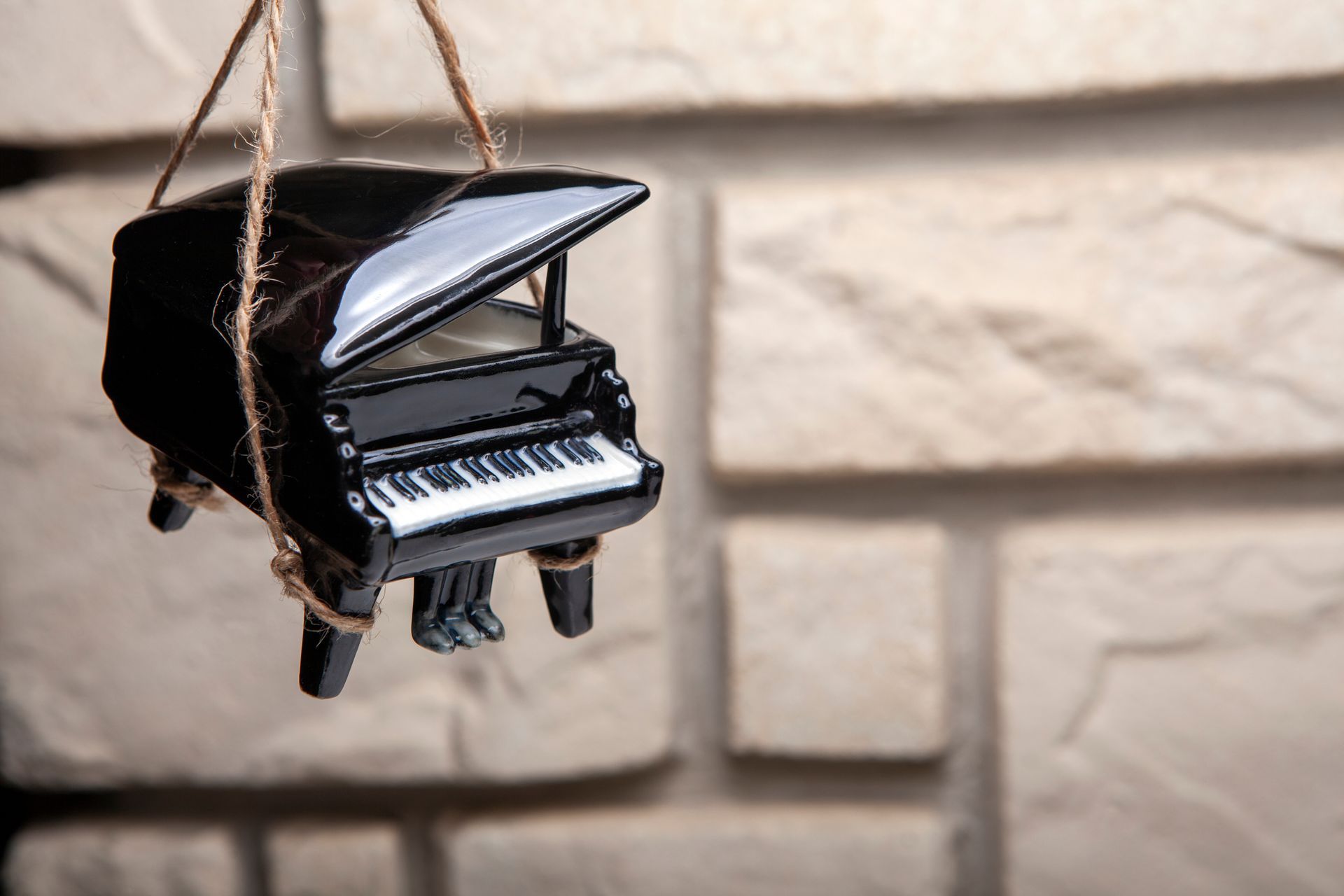 Small black grand piano ornament hanging by twine against a light brick wall background.