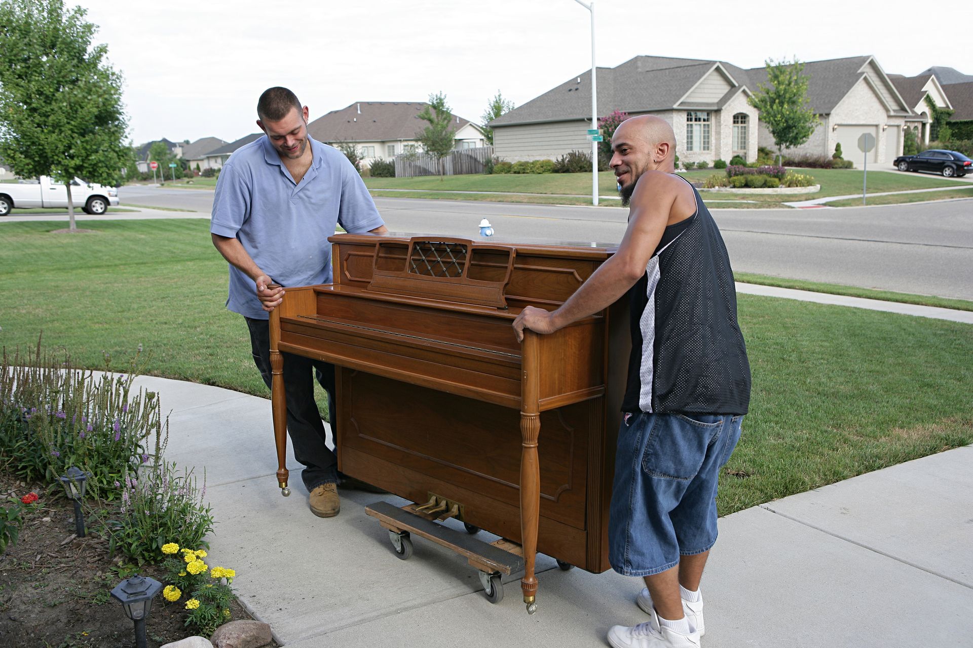 Two men carefully moving a piano in a neighborhood during a professional piano haul-away service.
