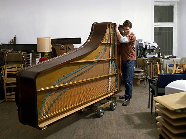 A man beside a piano in a living room, preparing for a piano haul away with care and purpose.