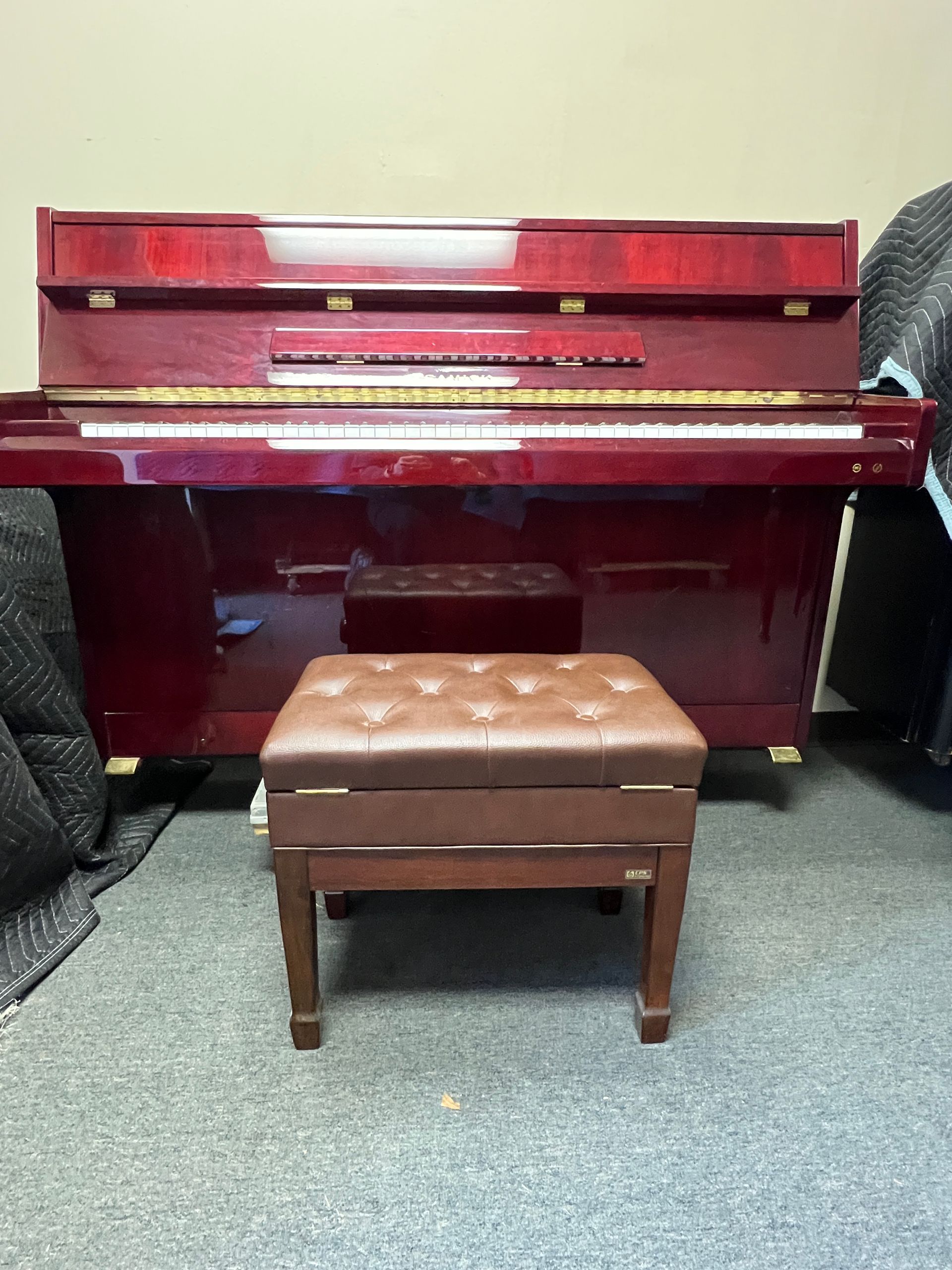A maroon piano with a brown leather-topped stool in front.