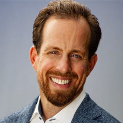 A man with a beard and a blue jacket is smiling for the camera.