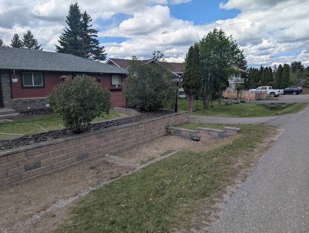 Residential area with a retaining wall, grass, and a road under a cloudy sky.