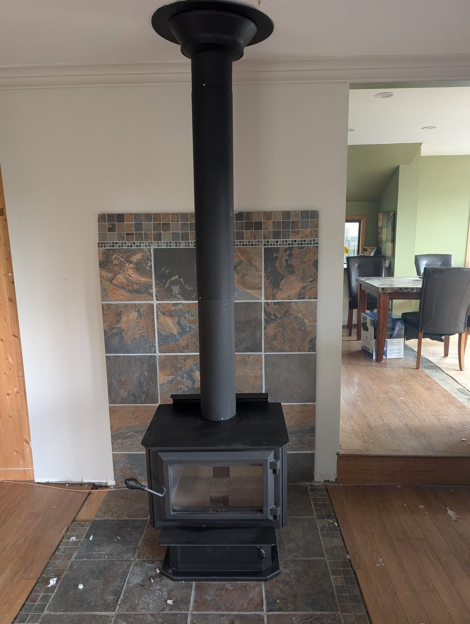 Wood-burning stove with black chimney, set on tiled hearth, mounted on a wall with decorative tiles; interior.