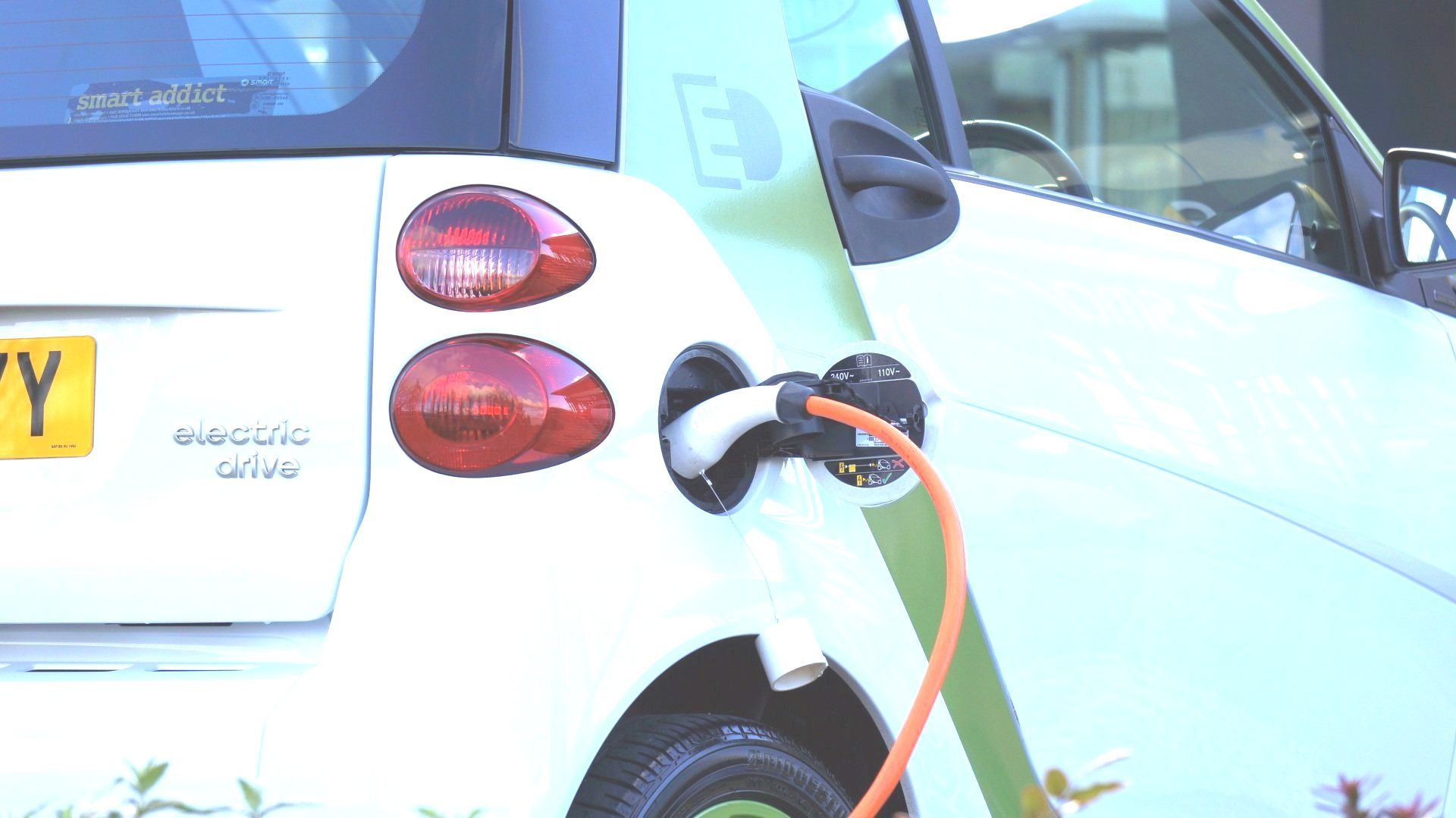 a white electric car is being charged with an orange cord .