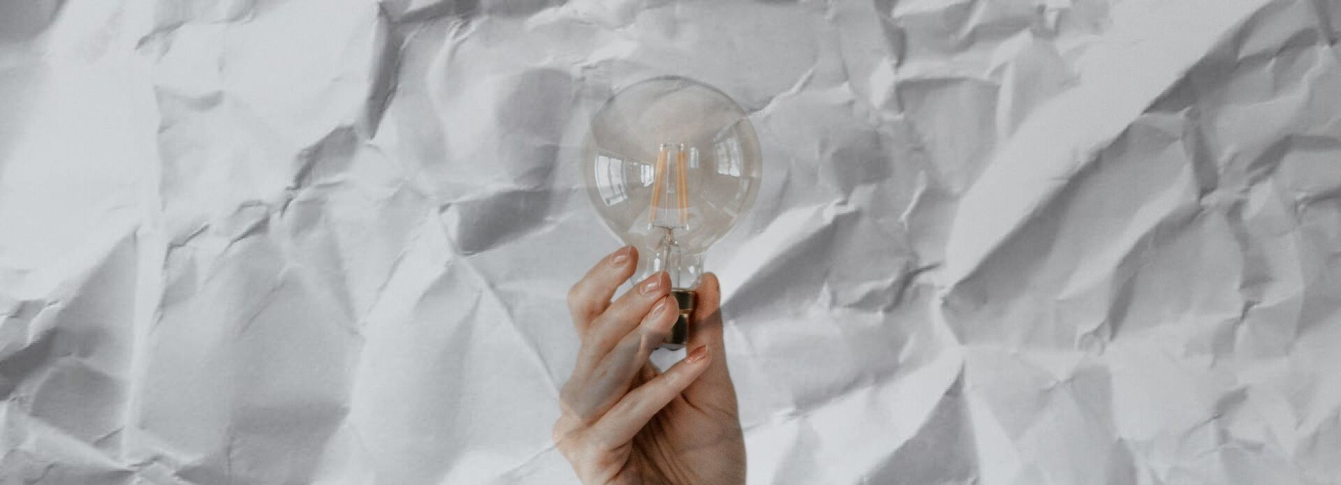 A person is holding a light bulb in their hand on a piece of crumpled paper.