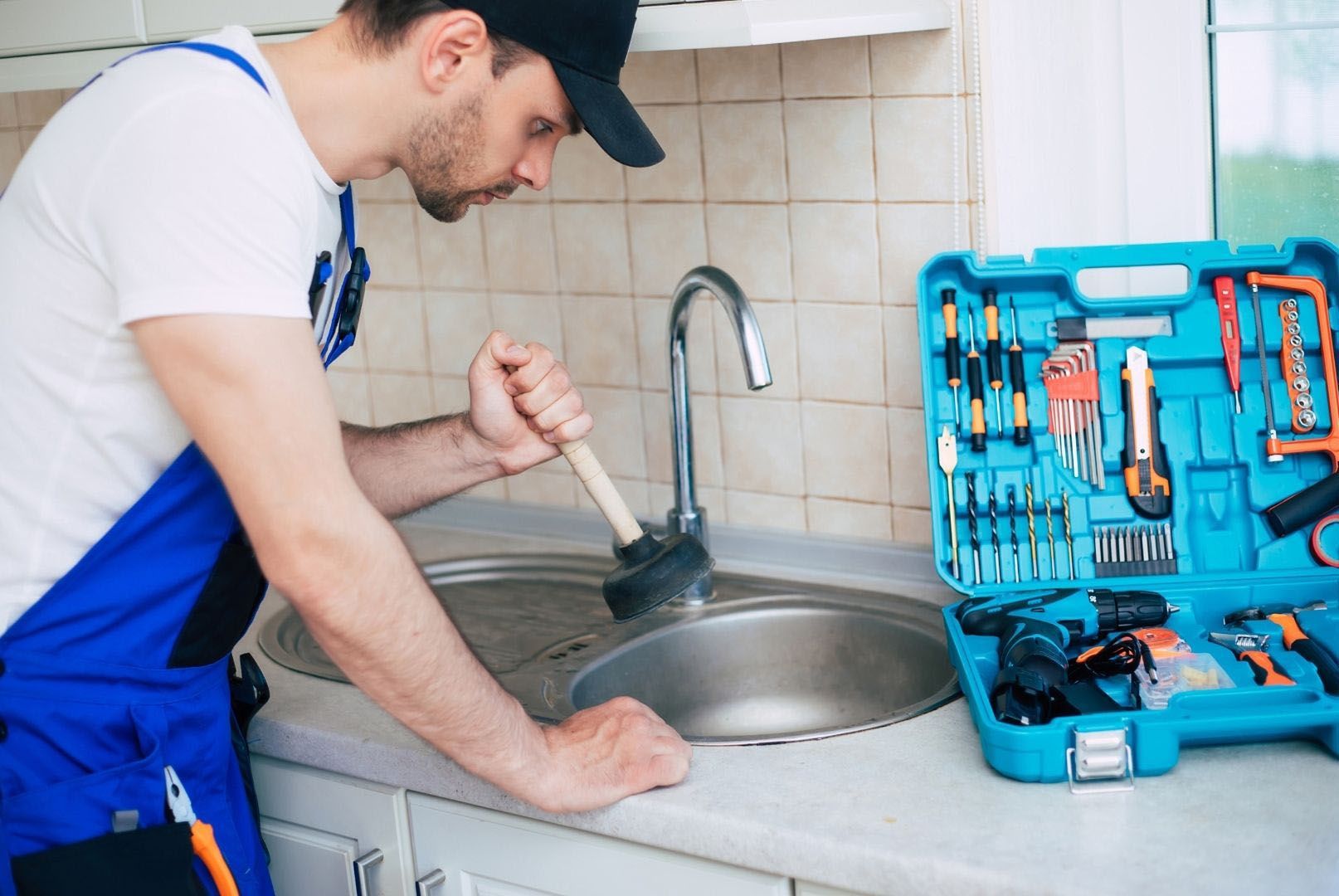 A man is fixing a sink in a kitchen with a plunger.