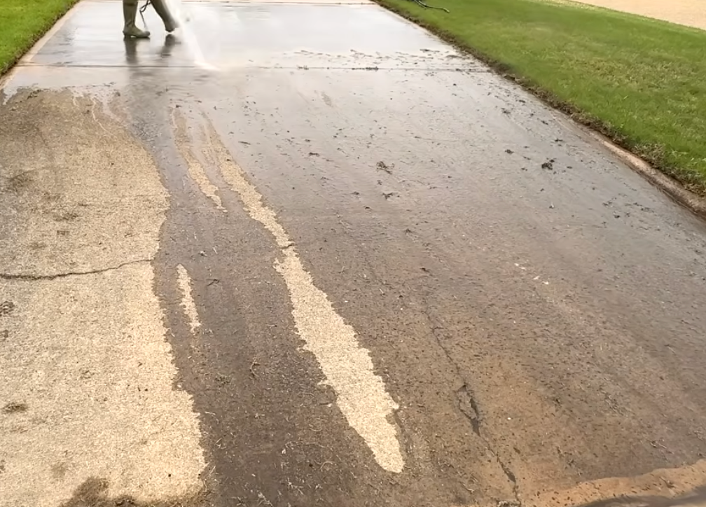A person is walking down a wet road with a pressure washer