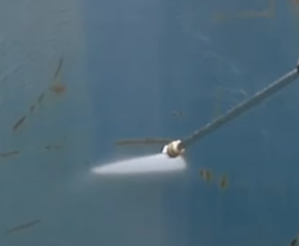 Close-up of pressure washer nozzle cleaning pool deck.