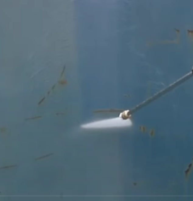 A person is using a high pressure washer to clean a blue wall.