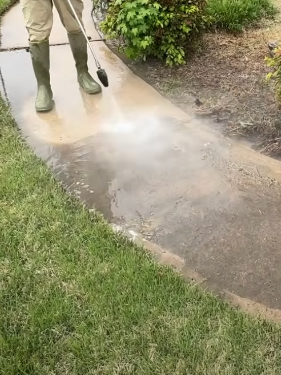 A person is using a pressure washer to clean a dirty sidewalk.