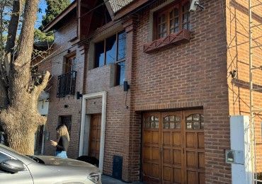 Casa de ladrillo con puerta de garaje de madera, pequeño balcón y una persona parada cerca de la entrada.