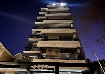 Edificio de apartamentos de varias plantas de noche, con balcones y un cielo azul oscuro. Se ve el número 927.